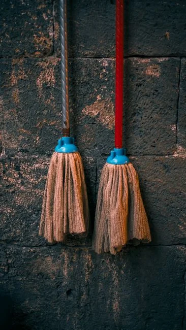 Cheerful woman with headphones singing and cleaning the living room with a mop.